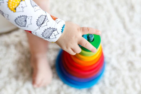 Adorable cute beautiful little baby girl playing with educational wooden toys at home or nursery. Toddler with colorful stack pyramid and music toy. Happy healthy child having fun with different toysの写真素材