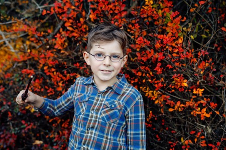 Beautiful kid boy in costume as a magician. Happy healthy child celebrating Halloween. Boy with glasses outdoors on autumn day.の写真素材