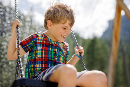 Funny kid boy having fun with chain swing on outdoor playground while being wet splashed with water. child swinging on summer day. Active leisure with kids. Happy crying boy with rain drops on face.の写真素材