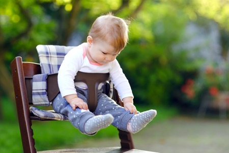 Cute adorable baby girl sitting in high chair outdoors. Beatuiful child of 6 months in home garden, playing on warm sunny day. Healthy baby smiling and laughing.の写真素材
