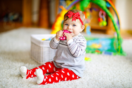 Adorable baby girl playing with educational toys in nursery. Happy healthy child having fun with...