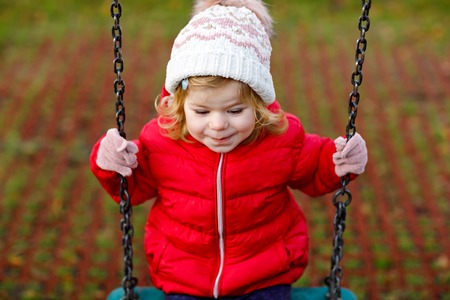 Cute toddler girl having fun on playground. Happy healthy little child climbing, swinging and sliding on different equipment. On cold day in colorful clothes. Active outdoors game for childrenの写真素材