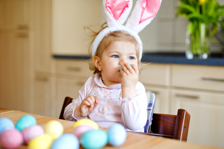 Cute little toddler girl wearing Easter bunny ears playing with colored pastel eggs. Happy baby child unpacking gifts. Adorable healthy smiling kid in pink clothes enjoying family holidayの写真素材