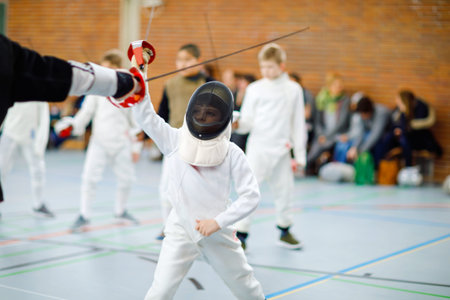 Little kid boy fencing on a fence competition. Child in white fencer uniform with mask and sabre....