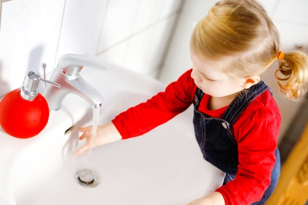 Cute little toddler girl washing hands with soap and water in bathroom. Adorable child learning cleaning body parts. Morning hygiene routine. Happy healthy kid at home or nursery.の写真素材