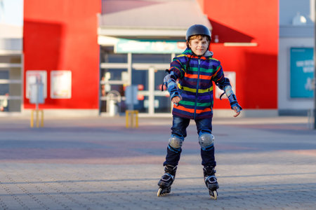Cute school kid boy skating with rollers in the city. Happy healthy child in protection safety...