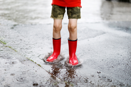 Child wearing red rain boots jumping into a puddle.の写真素材
