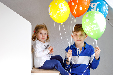 Portrait of happy kid boy and cute little toddler girl with bunch on colorful air balloons on birthday. Smiling happy school child and sister having fun, celebrating birthday. Family partyの写真素材