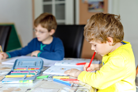 Two little kids boys at home making homework. Little concentrated children writing with colorful pencils, indoors. Elementary school and education. Siblings and best friends learning.の写真素材