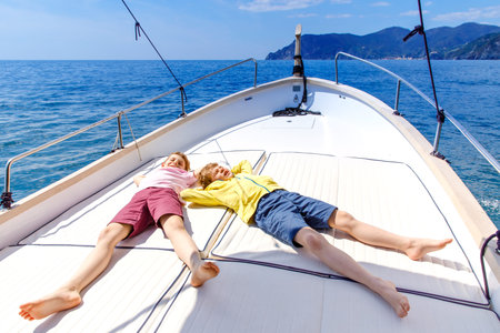 Two little kid boys, best friends enjoying sailing boat trip. Family vacations on ocean or sea on sunny day. Children smiling. Brothers, schoolchilden, siblings having fun on yacht.の写真素材