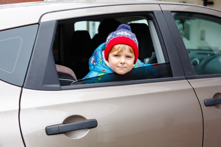 Portrait of pretty toddler boy sitting in car seat. Child transportation safety. Cute healthy kid boy looking happy about family vacations with car through window during standing in traffic jamの写真素材