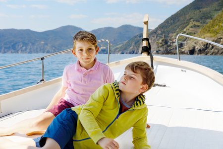 Two little kid boys, best friends enjoying sailing boat trip. Family vacations on ocean or sea on sunny day. Children smiling. Brothers, schoolchilden, siblings, best friends having fun on yacht.の写真素材
