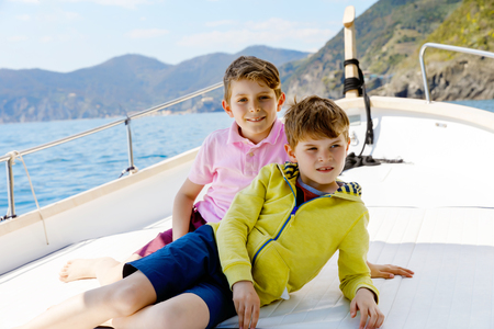Two little kid boys, best friends enjoying sailing boat trip. Family vacations on ocean or sea on sunny day. Children smiling. Brothers, schoolchilden, siblings, best friends having fun on yacht.の写真素材