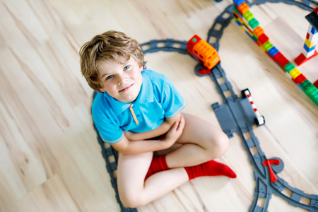 little blond kid boy playing with colorful plastic blocks and creating train stationの写真素材