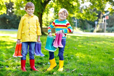 Two little kids boys, cute siblings with lots of colorful rain boots. Children in different rubber boots and jackets. Footwear for rainy fall. Healthy twins and best friends having fun outdoorsの写真素材