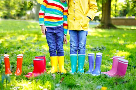 Little kids, boys and girls in colorful rain boots. Close-up of children in different rubber boots, jeans and jackets. Footwear for rainy fallの写真素材