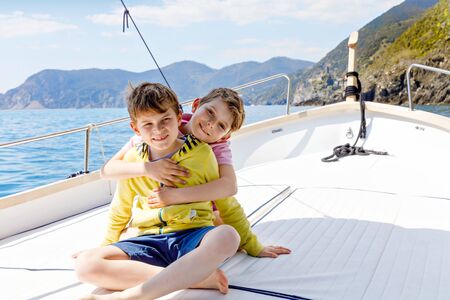 Two adorable school kid boys, best friends enjoying sailing boat trip. Family vacations on sea on sunny day. Children smiling. Brothers, schoolchilden, siblings, best friends having fun on yacht.の写真素材