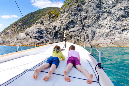 Two adorable school kid boys, best friends enjoying sailing boat trip. Family vacations on sea on sunny day. Children smiling. Brothers, schoolchilden, siblings, best friends having fun on yacht.の写真素材