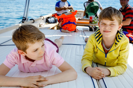 Two little kid boys, father and toddler girl enjoying sailing boat trip. Family vacations on ocean or sea on sunny day. Children smiling. Brothers and sister, siblings and dad having fun on yacht.の写真素材