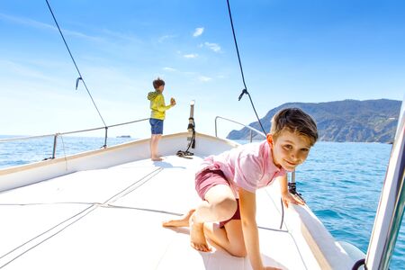 Two little kid boys, best friends enjoying sailing boat trip. Family vacations on ocean or sea on sunny day. Children smiling. Brothers, schoolchilden, siblings, best friends having fun on yacht.の写真素材