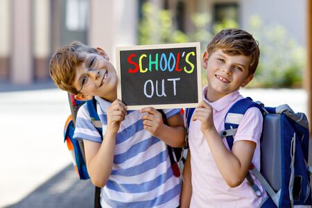 Two little kid boys with backpack or satchel. Schoolkids on the way to school. Healthy children, brothers and best friends outdoors on street leaving home. Schools out on chalk desk. Happy siblings.の写真素材