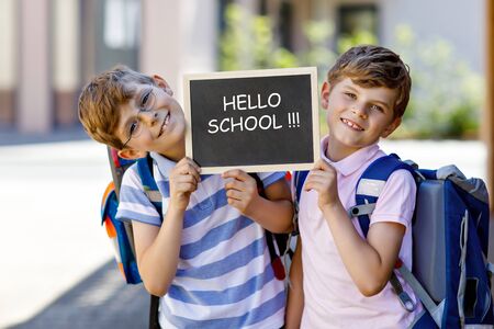 Two little kid boys with backpack or satchel. Schoolkids on the way to school. Healthy children, brothers and best friends outdoors on street. Hello school on chalk desk. Happy siblingsの写真素材