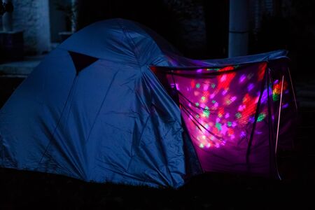 Tent with children inside glow in the night. Kids making overnight sleeping party in domestic garden. Adventure in summer vacationsの写真素材