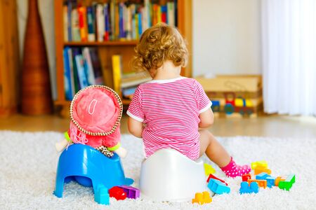 Closeup of cute little 12 months old toddler baby girl child sitting on potty. Kid playing with doll toy. Toilet training concept. Baby learning, development stepsの写真素材