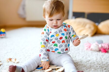 Gorgeous cute beautiful little baby girl playing with educational toys like wooden puzzle at home or nursery. Happy healthy child having fun with colorful different toys. Kid learning different skillsの写真素材
