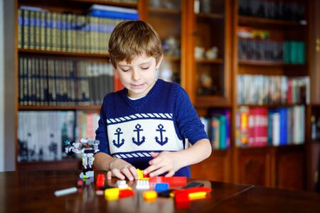 Little blond child playing with lots of colorful plastic blocks. Cute school kid boy having fun with building and creating robot. Creative leisure modern technic and robotic.の写真素材