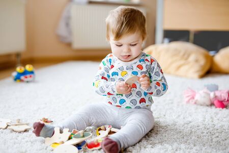 Gorgeous cute beautiful little baby girl playing with educational toys like wooden puzzle at home or nursery. Happy healthy child having fun with colorful different toys. Kid learning different skillsの写真素材