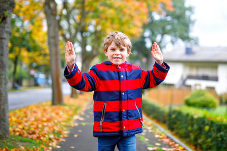 Happy little boy running on autumnal street after school. Kid happy about school vacations. Child...