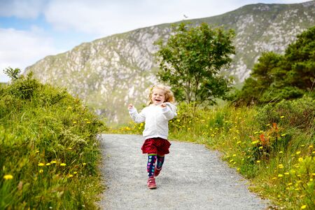 Cute little happy toddler girl running on nature path in Glenveagh national park in Ireland. Smiling and laughing baby child having fun spending family vacations in nature. Traveling with small kidsの写真素材