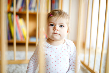 Beautiful little baby girl standing inside playpen. Cute adorable child playing with colorful toys....