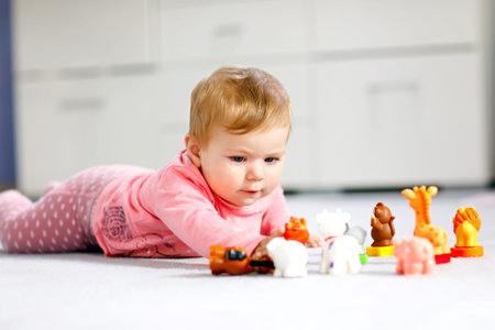 Adorable baby girl playing with domestic toy pets like cow, horse, sheep, dog and wild animals like...