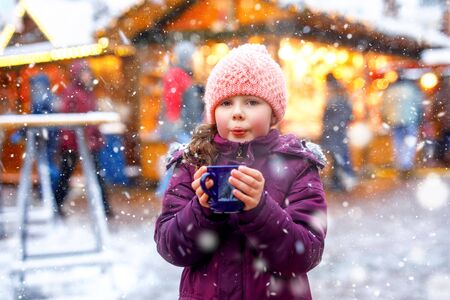 Little cute kid girl with cup of steaming hot chocolate or children punch. Happy child on Christmas market in Germany. Traditional leisure for families on xmas.の写真素材