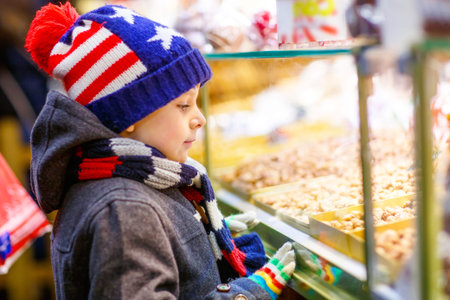Little cute kid boy near sweet stand with gingerbread and nuts. Happy child on Christmas market in...