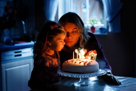 Adorable little toddler girl celebrating third birthday. Baby child daughter and young mother blowing candles on cake and candles. Happy healthy family portrait, mom love and happiness.の写真素材
