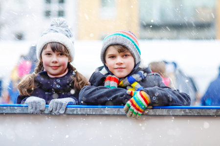 Two happy little kids girl and boy in colorful warm clothes skating on a rink of Christmas market or fair. Healthy children having fun on ice skate. Lot of people having active winter leisure.の写真素材