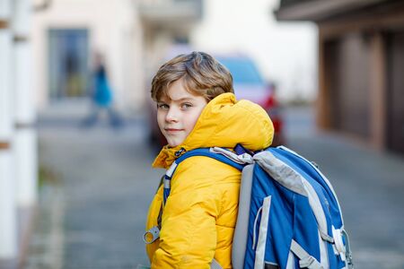 Little school kid boy of elementary class walking to school. Portrait of happy child on the street with traffic. Student with in yellow jacket and backpack in colorful winter clothes.の写真素材