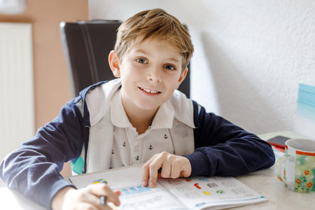 Portrait of cute happy school kid boy at home making homework. Little child writing with colorful...