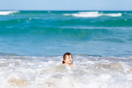 Adorable little blond kid boy having fun on ocean beach. Excited child playing with waves, swimming, splashing and happy about family vacations in Miami, Florida, USA..の写真素材
