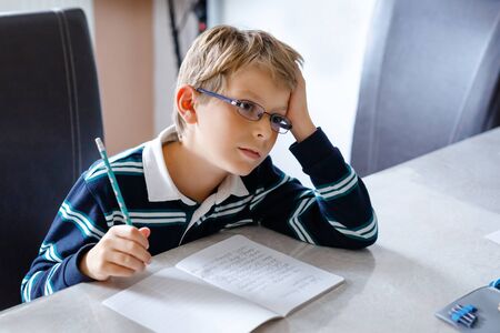 Thoughtful little kid boy with glasses at home making homework, writing text with colorful pens. Little child doing exercise, indoors. Elementary school and educationの写真素材