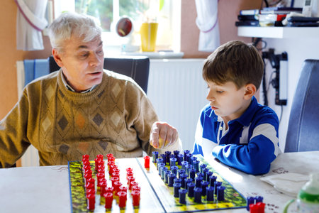 Grandfather and school kids boy playing strategy table game together. Senior man having fun with his...