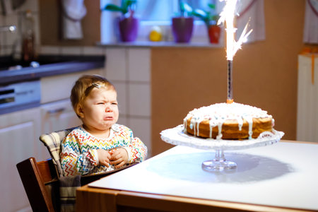 Cute crying little baby girl celebrating first birthday. Child scared and afraid of firework on...