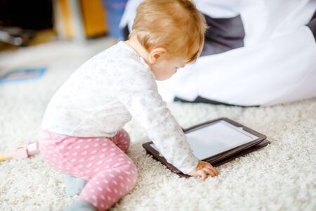 Cute adorable baby girl watching cartoons on tablet pc. Todder child at home touching on screen and playing educational games on computerの写真素材