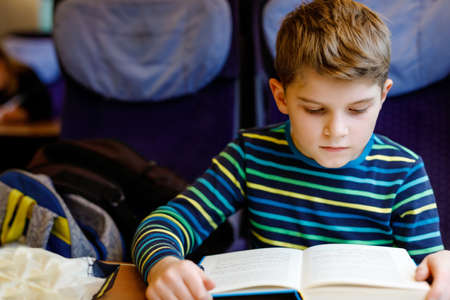 Cute adorable kid boy reading book during traveling by train. Happy child sitting near window. Family going on vacations. Active leisure during a journey trip.の写真素材