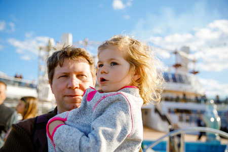 Happy cute little toddler girl on arms of dad on cruise ship. Adorable baby child and father,...