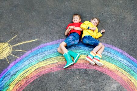 two school kids boys with rainbow painted with colorful chalks on ground during pandemic coronavirus quarantine. Children painting rainbows along with the words Lets all be well.の写真素材
