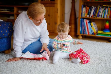 Cute little toddler girl and grandmother playing with toys at home. Adorable baby child and senior retired woman unpacking gifts for birthday. Happy family togetherの写真素材